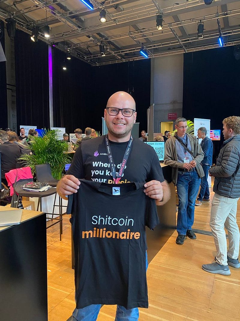 An Ambire employee holding a t-shirt saying Shitcoin Millionaire at an event